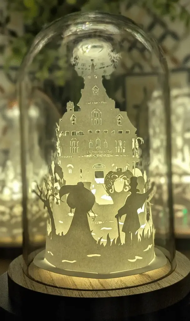 Cloche lumineuse artisanale en papier représentant une maison hantée et des personnages féeriques – création Halloween par L’atelier de Mannastrel.